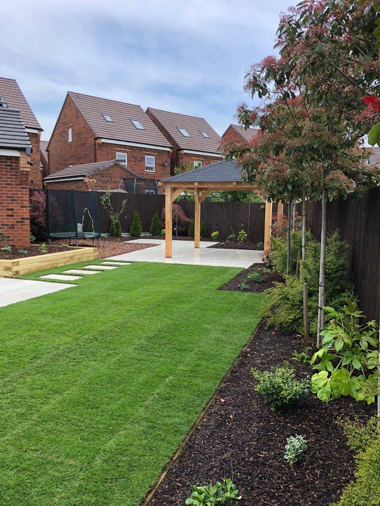 Garden with a wooden gazebo, grass, and plants in front of houses