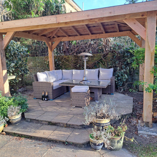 A sturdy wooden gazebo covering a sofa set on a patio against a garden wall