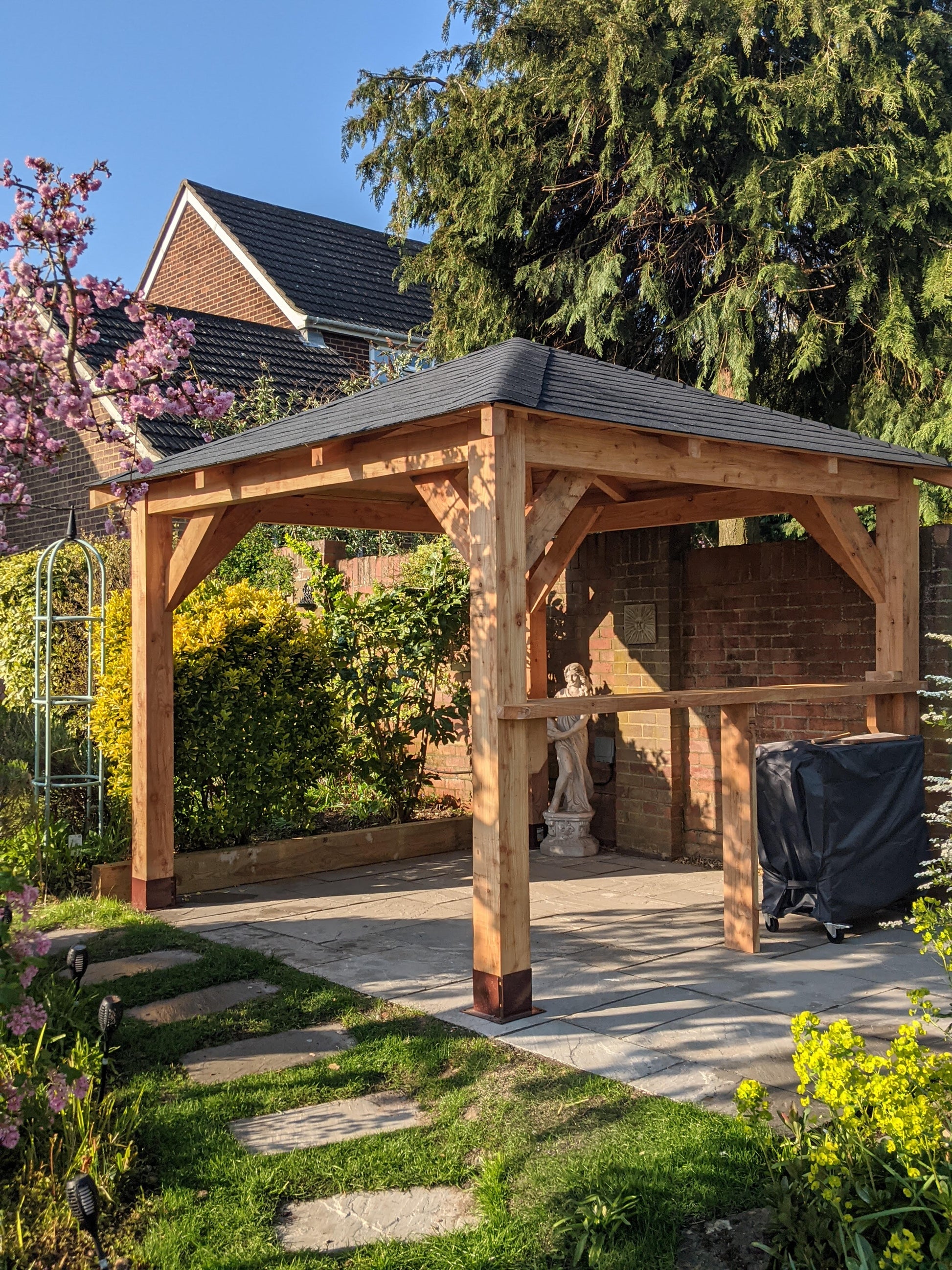 Wooden gazebo in a garden setting with a house in the background