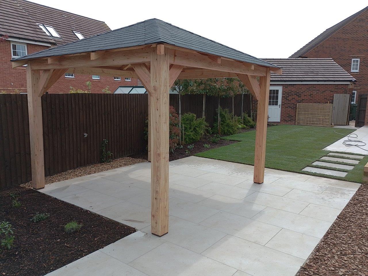 Wooden larch forester gazebo on a patio with houses in the background