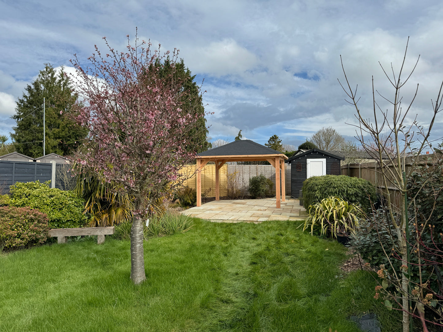 Garden scene with a wooden gazebo, trees, and lush green grass.