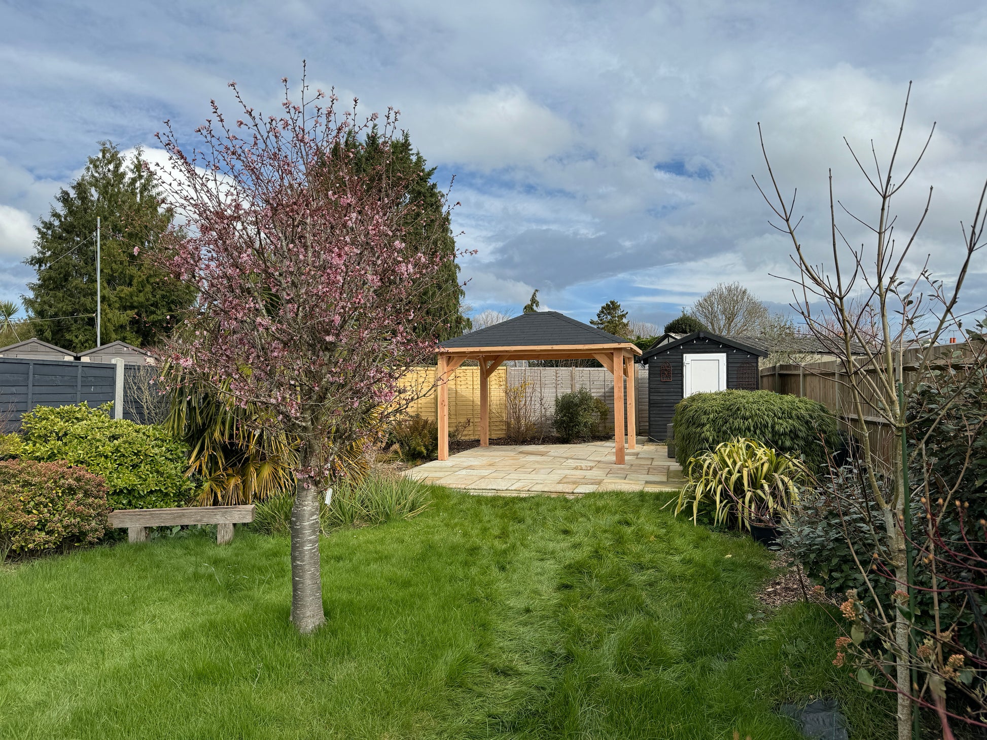 Garden scene with a wooden gazebo, trees, and lush green grass.
