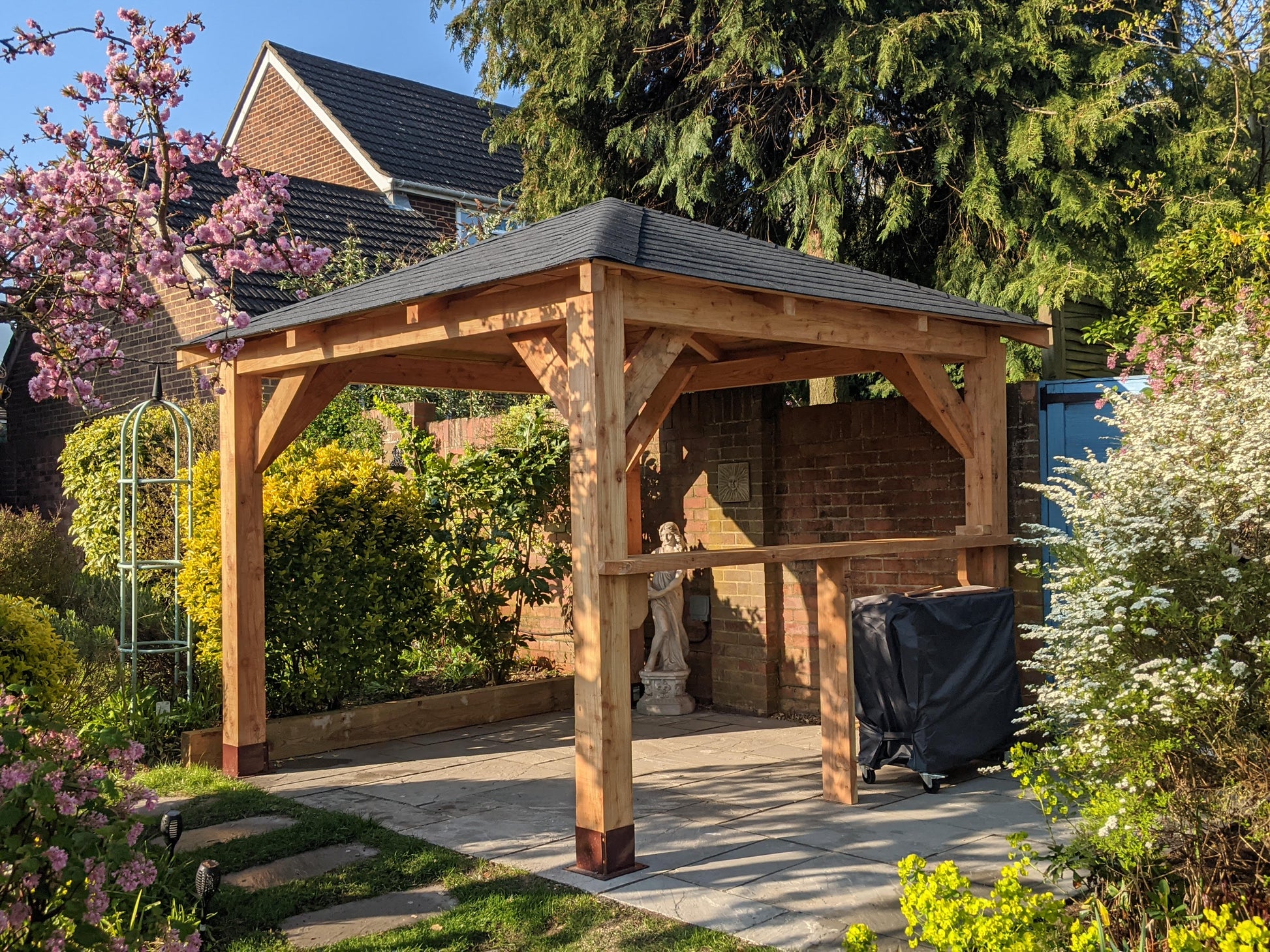 Wooden gazebo in a garden setting with flowers and trees