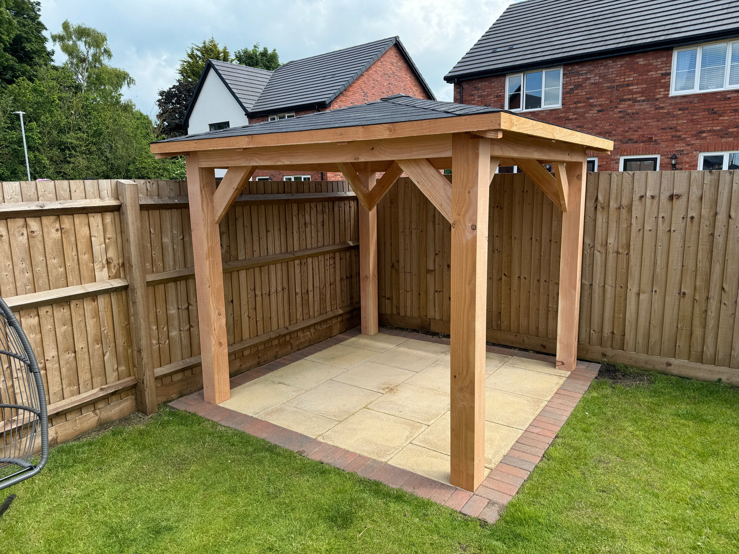 Wooden gazebo on a grassy area with a house in the background